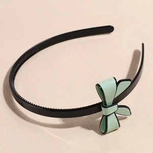 Detail of mint green bow headband with black trim and anti-slip teeth on a beige surface