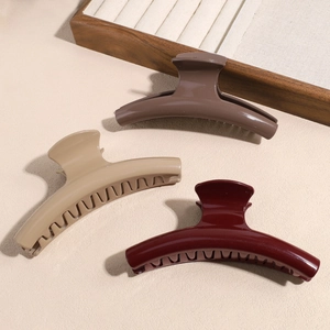 Three-piece large hair claw clips in glossy brown, cream and burgundy set on a textured surface