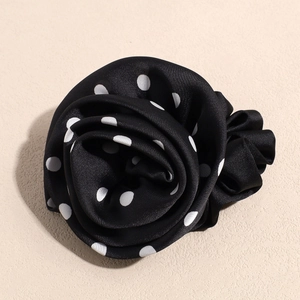 Gros plan sur le chouchou en satin à pois noir et blanc en forme de fleur de rose