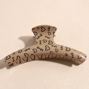 Detail of khaki hair claw clip with black heart and LOVE print on a textured background