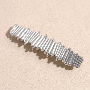 Dettaglio macro di un fermaglio per capelli argento con trama 3D ondulata e metallica