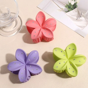 Trois pinces à cheveux fleurs mates avec strass en rose, violet et vert sur fond texturé