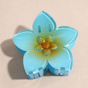 Détail d'une pince à cheveux en résine bleu clair avec une fleur orange au centre
