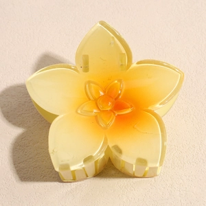 Détail macro d'une pince à cheveux en résine en forme de fleur jaune et orange dégradé