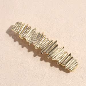 Dettaglio del fermaglio per capelli in metallo dorato con design a superficie ondulata