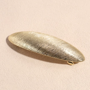 Dettaglio del fermaglio per capelli ovale dorato in lega con texture in metallo spazzolato