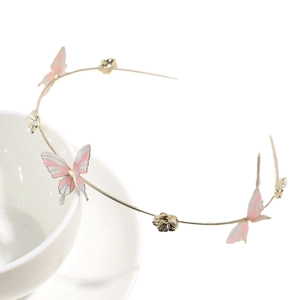 Gold-tone thin metal headband with pink butterfly accents on a white porcelain cup