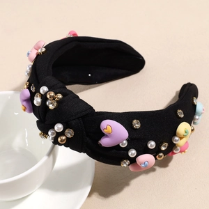 Detail of a black knotted headband with colorful crystal hearts and white pearls