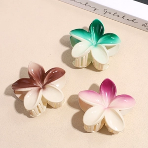 Three gradient floral hair claws in green, brown and pink colors on textured surface