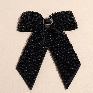 Detailed macro shot of a black bow hair clip with faux pearls and rhinestone center