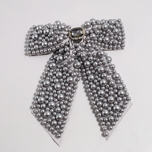 Close-up of grey pearl bow hair clip with central gemstone and sparkling rhinestone border