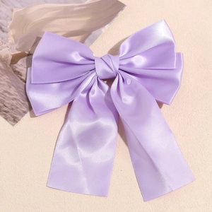 Detail of the elegant layered satin light purple bow hair clip on a textured beige surface