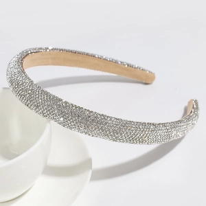 Close-up of sparkling full rhinestone headband with beige velvet lining on white ceramic cup