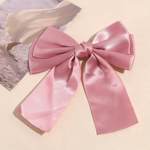 Detail of pink satin double-layered bow hair clip with elegant long ribbons on beige base