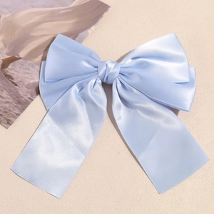 Detail of light blue satin double bow hair clip with elegant long ribbons on beige background