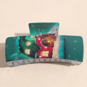 Detail of teal Christmas hair claw clip featuring festive red cabin and snowy tree patterns