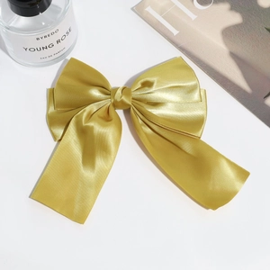Detailed macro view of a large golden satin double-layered bow hair clip on white surface