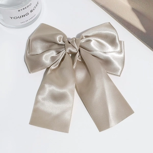 Close-up of champagne gold double-layered satin bow hair clip on a clean white desk