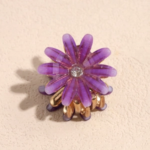 Makroaufnahme einer violetten Gänseblümchen-Haarklammer mit Kristall und Gold-Metall-Basis