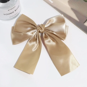 Detailed top view of large champagne gold satin bow hair clip on a minimalist white surface