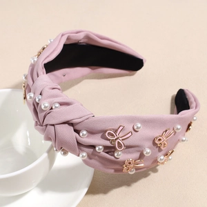 Detail eines rosa geknoteten Stirnbands mit weißen Perlen und rosa Emaille-Schleifen