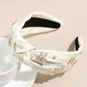 Detail eines cremefarbenen Satin-Haarreifs mit weißen Perlen und goldenen Emaille-Schleifen