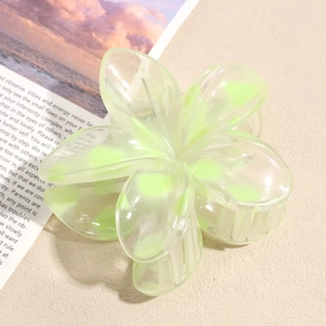 Detail of a translucent light green flower hair claw clip on a textured beige surface