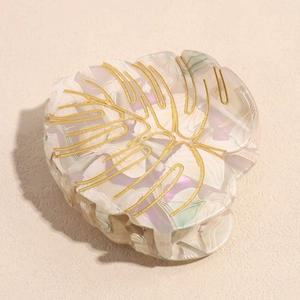 Close-up of leaf-shaped acetate hair claw with golden veins and marble texture