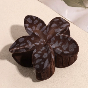 Close-up of brown flocked floral hair claw clip with grey spots on a beige surface