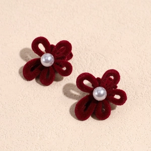 Dettaglio di fermagli a fiore in velluto rosso con perla centrale su fondo beige