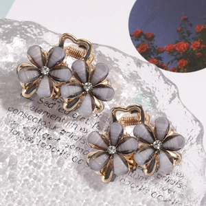 Close-up of grey camellia hair claws with rhinestone centers and golden heart handles