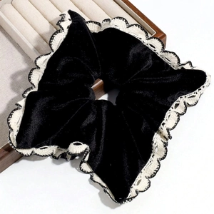 Detail of black velvet scrunchie with white lace edges on a wooden display stand