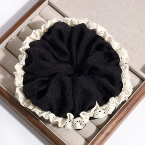 Detailed close-up of a black fabric hair scrunchie with cream lace trim in a wooden box