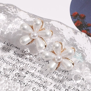 Close-up of elegant camellia flower earrings with white teardrop pearls on a textured background