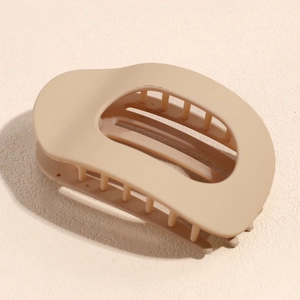 Vue détaillée d'une pince à cheveux mate beige ovale avec un grand design creux en forme de D