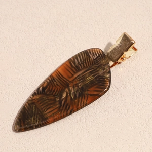 Detail of amber acetate hair clip with golden metal base on a beige textured background