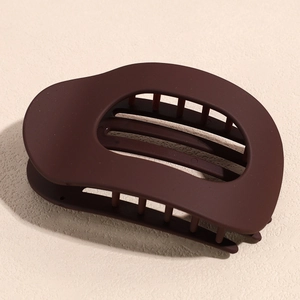 Détail d'une pince à cheveux marron mat avec un design ovale évidé et une prise dentelée