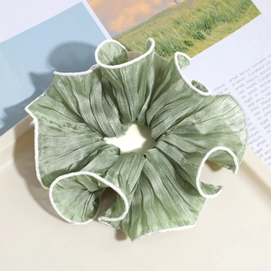 Close-up of Morandi green linen hair scrunchie with white pleated edges on a tray