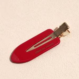 Detail of red acetate duckbill clip with gold Creation France lettering on textured base