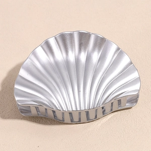 Close-up of silver shell-shaped hair claw clip with metallic finish and striped texture