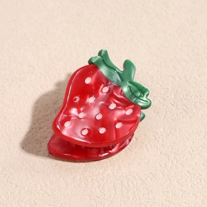 Macro detail of a red strawberry hair claw clip with white dots and green leaves