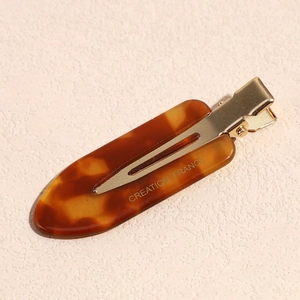Detailed close-up of tortoiseshell acetate hair clip with golden metal base and engraving