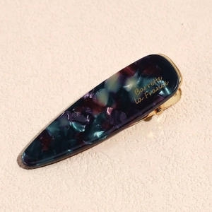 Detailed close-up of acetate hair clip with marble texture and gold metal fastening