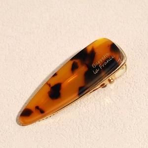 Detail showing tortoise shell acetate hair clip with golden metal clip and logo