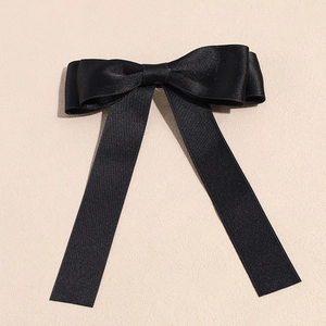 Close-up of elegant black satin ribbon bow hair clip with long streamers on beige surface