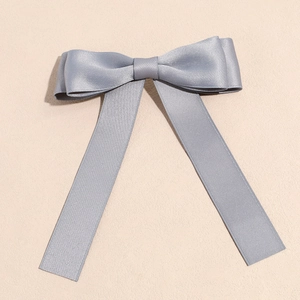 Detail of dark grey satin bow hair clip with elegant long ribbons on a beige background