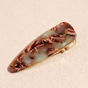 Detail of tortoiseshell acetate hair clip with golden metal base and artistic text