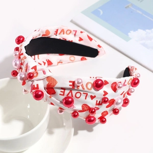 Detail eines weißen Knotenstirnbands mit Herzaufdruck und dekorativen Perlen