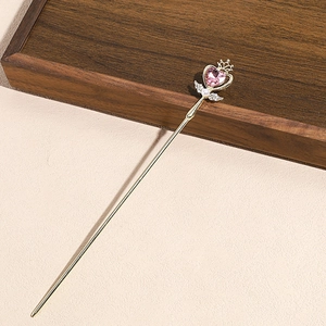 Close-up of golden hair pin with pink heart gem, pearl detail and tassel ornament