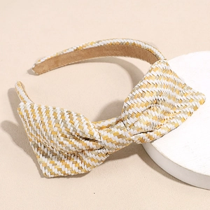 Detailopname van gele en groene raffia haarband met strik op een witte displaystandaard